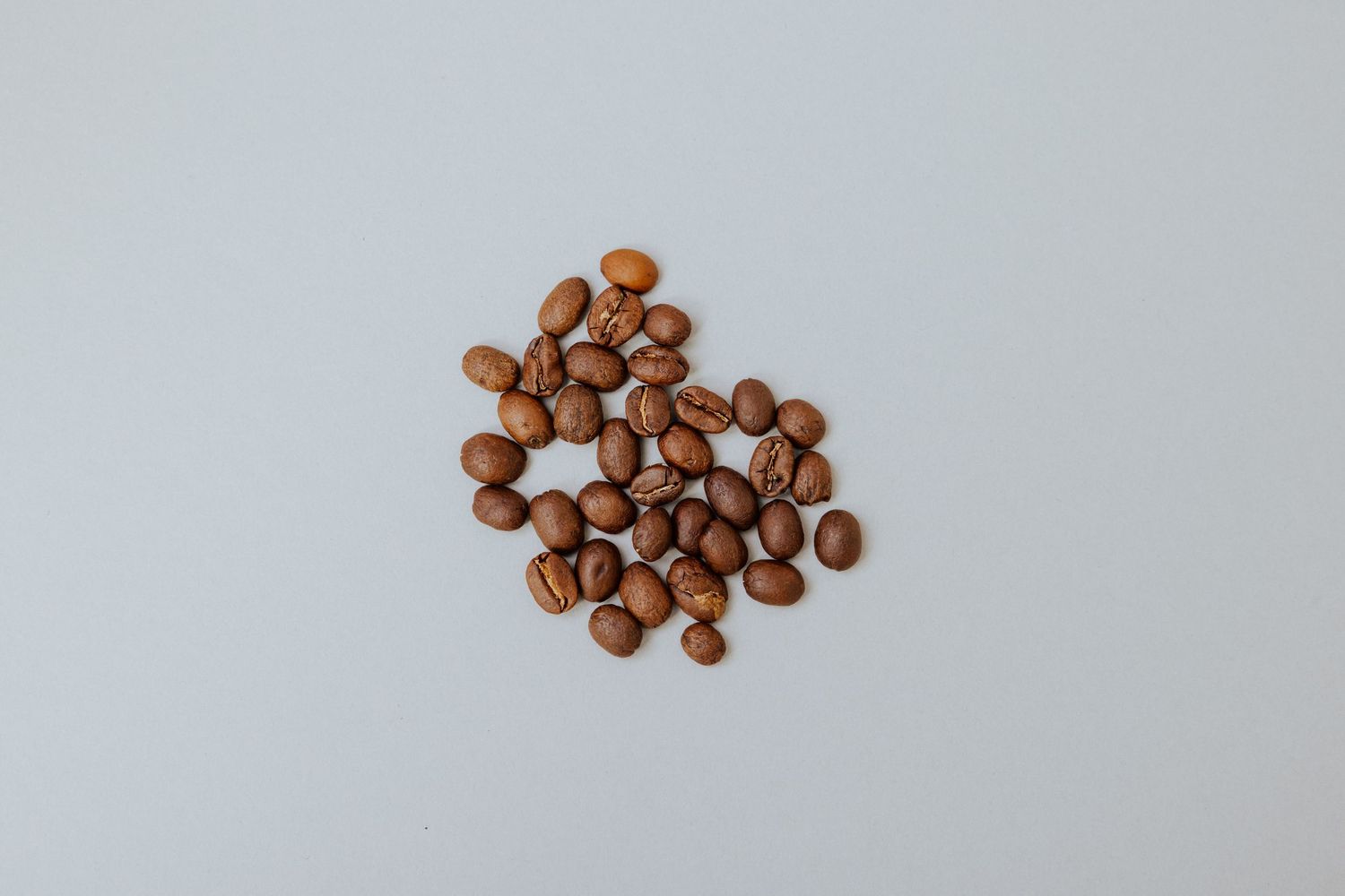 A small cluster of whole coffee beans scattered on a plain white surface.
