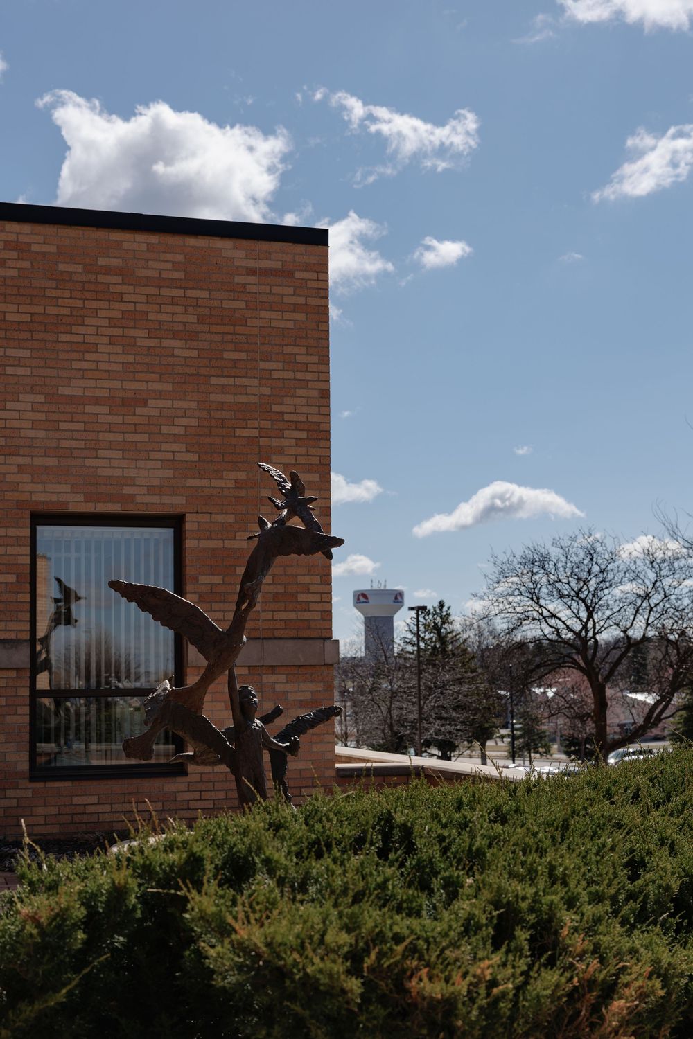 Brick building exterior against blue sky with trees and sculptural elements.