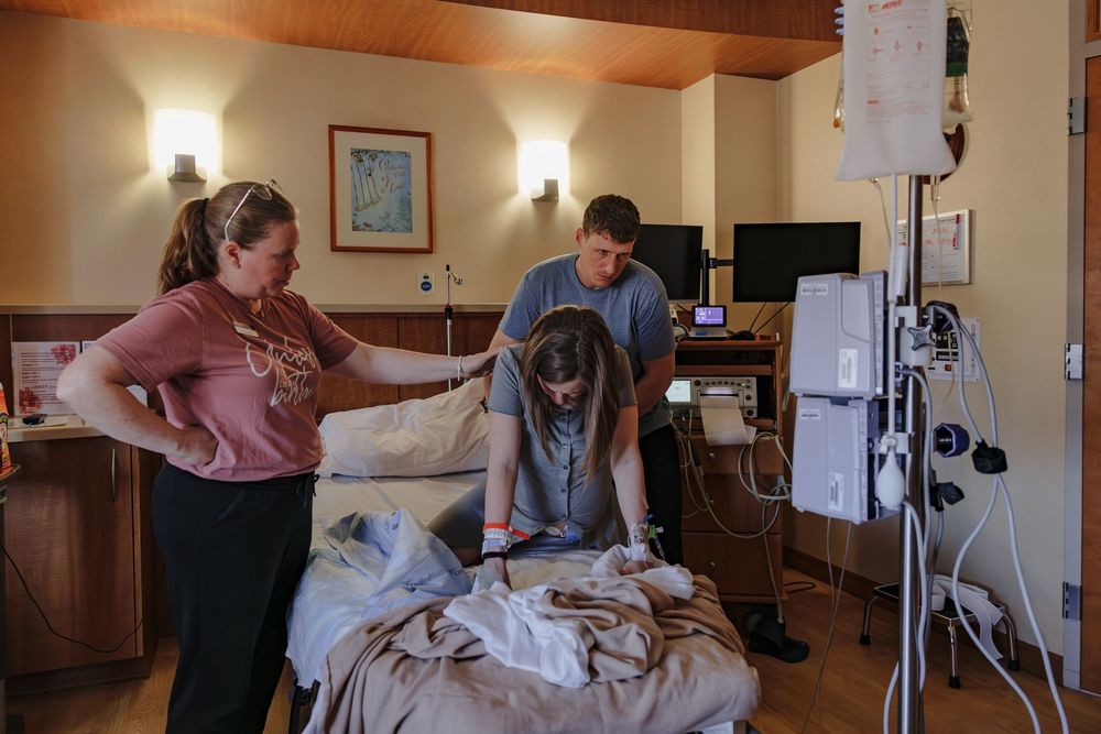 Medical staff tends to a patient in a hospital room with wood paneled walls and medical equipment.