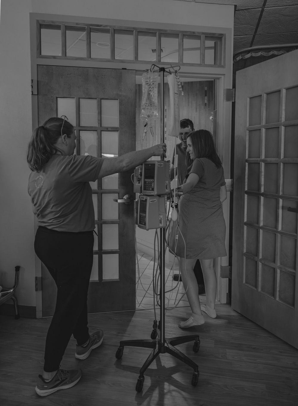 Two people setting up professional lighting equipment in a room with French doors.