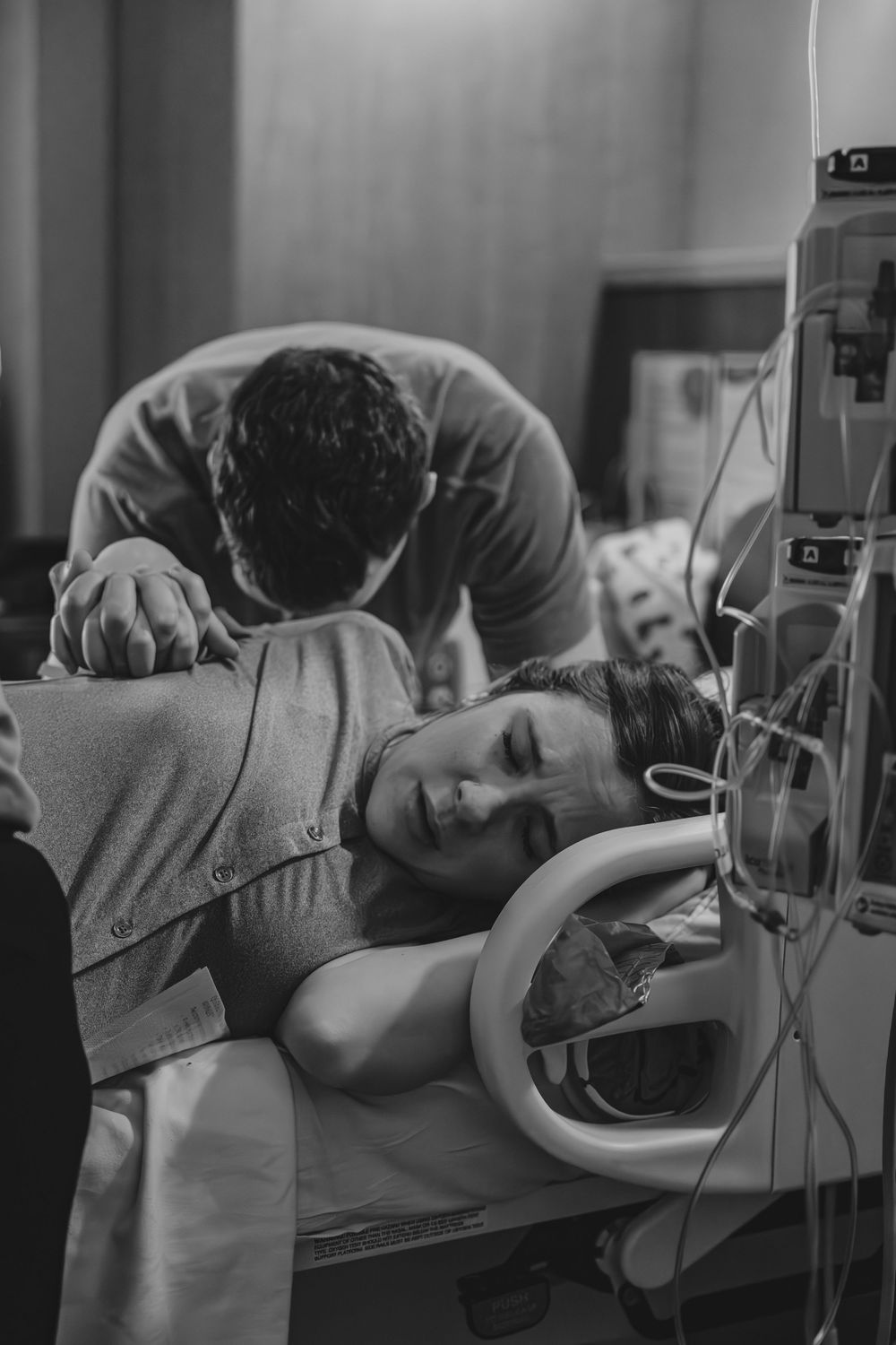 A black and white photo showing an emotional moment in a hospital room with medical equipment visible.
