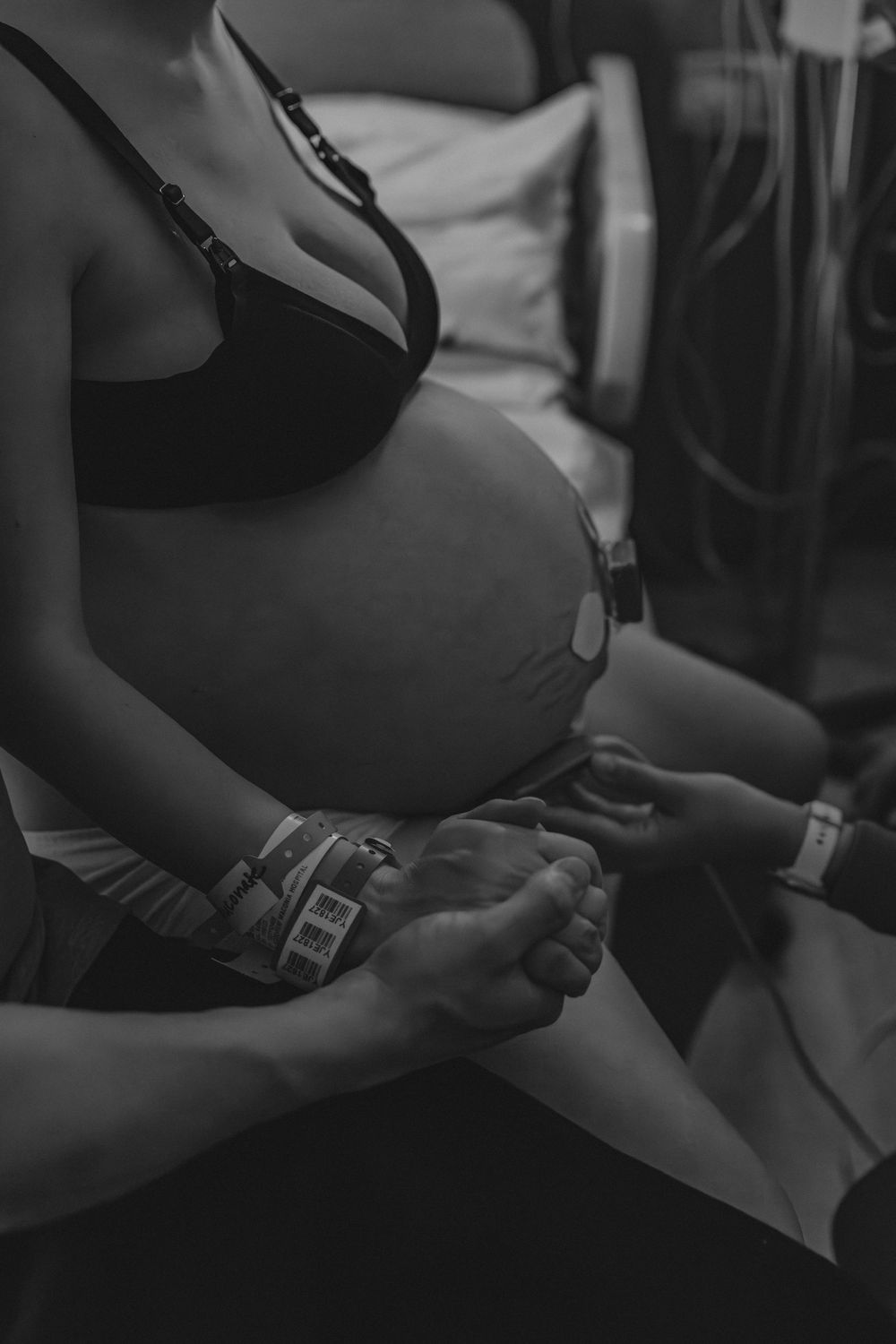 Black and white close-up of pregnant belly with hands clasped resting on hospital bed.