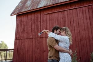 Romantic embrace in front of classic red barn exterior.