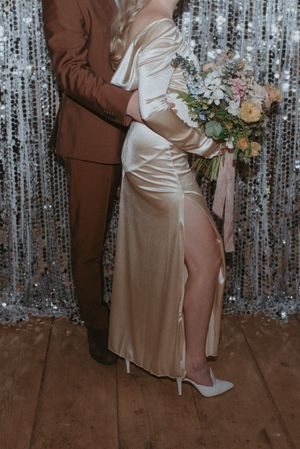 Detail shot of a couple in formal attire against a silver backdrop, showing a silk dress and brown suit.
