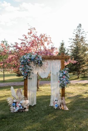 A wedding arch decorated with blue flowers, white fabric, and cherry blossoms stands in a spring garden.