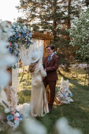 A couple shares an intimate moment under a floral-decorated arch at their outdoor wedding.