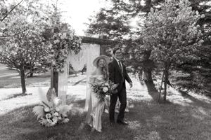Black and white wedding photo with macrame backdrop and floral arrangements in garden setting.