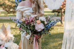 Close-up of pastel wedding bouquet with pink and blue flowers against cream dress.