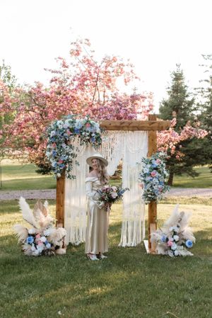 Outdoor wedding arch with white macrame, blue hydrangeas and cherry blossoms in spring garden setting.