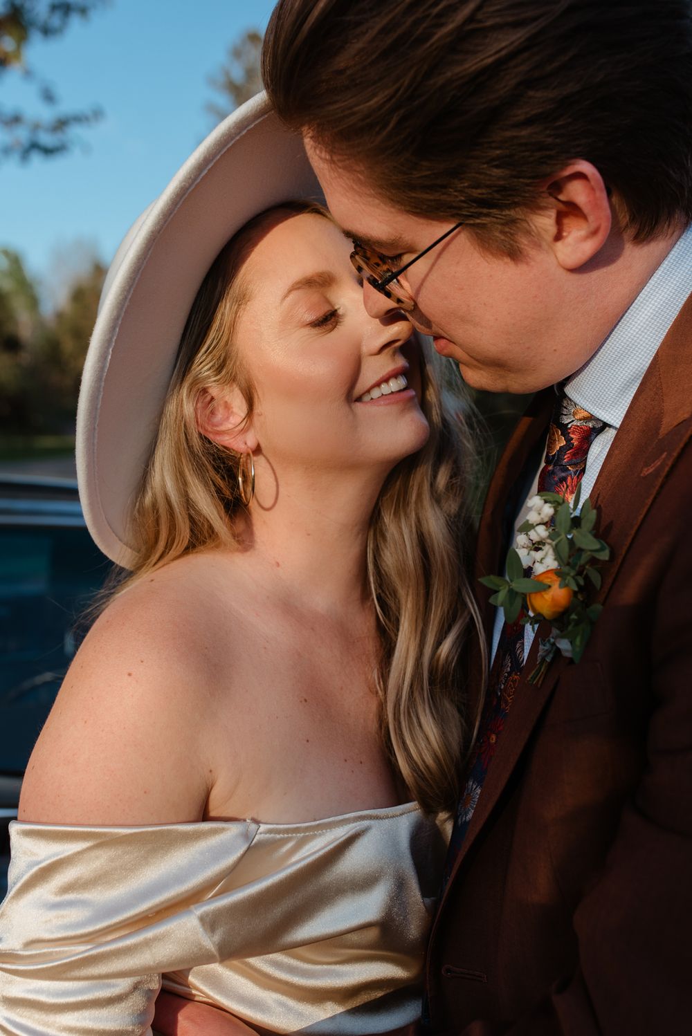 Tender moment between couple against classic car during sunset wedding shoot.