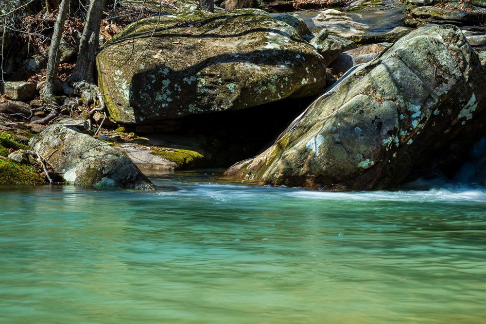 Clear turquoise water flows around large moss-covered boulders in a serene stream. Whitaker Creek