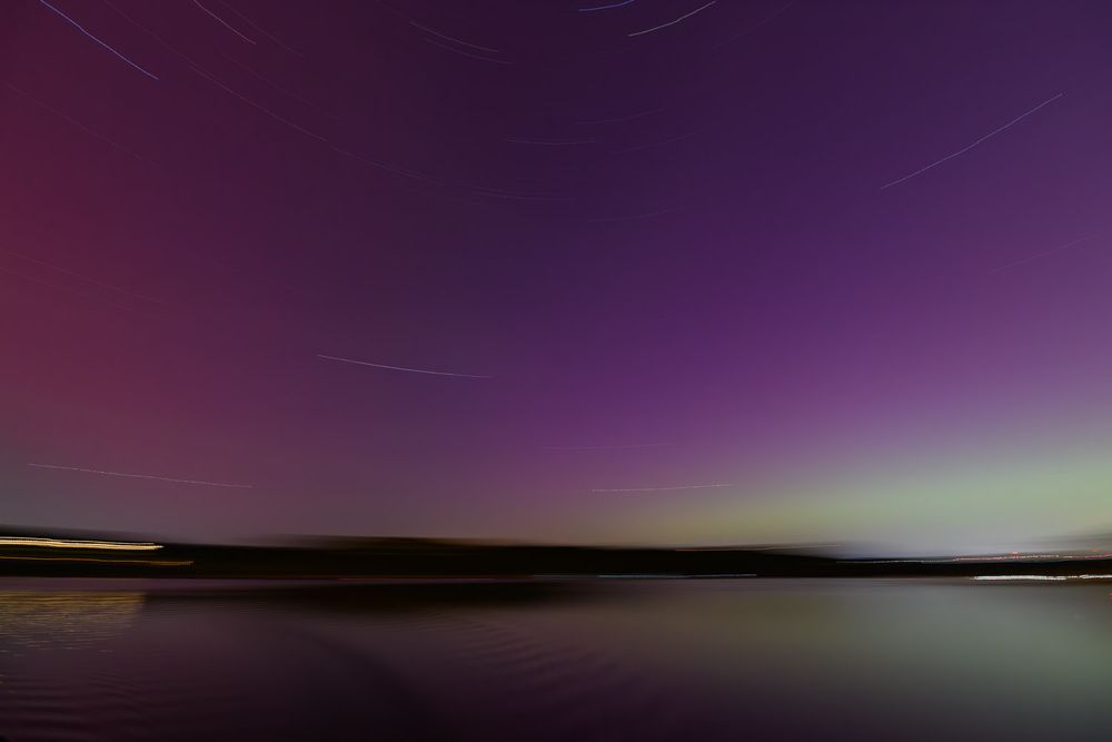 Northern lights aurora borealis glowing purple and green over a calm reflective Table Rock Lake. Long exposure