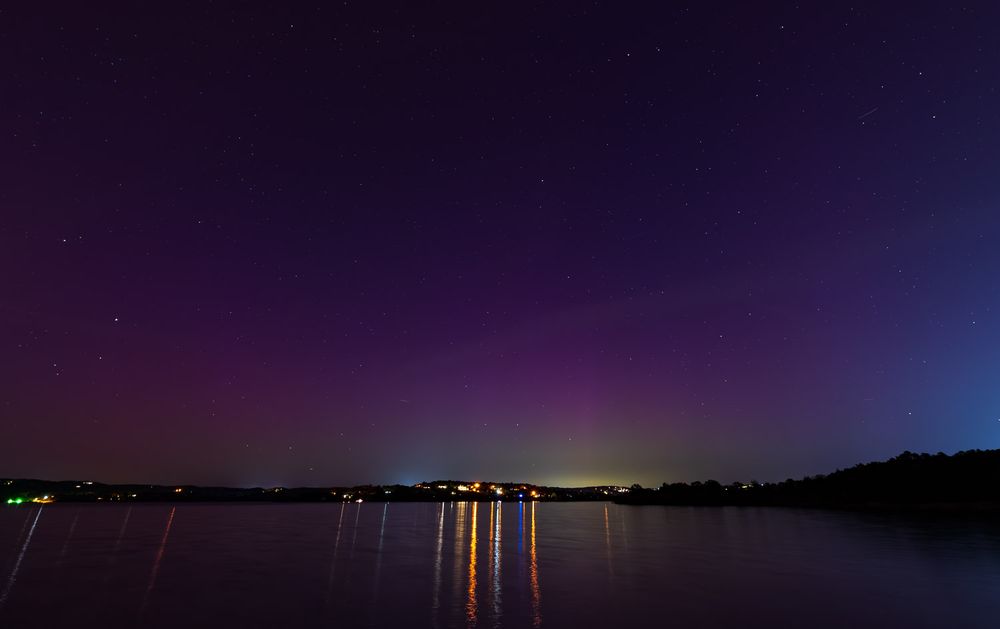 Aurora borealis illuminates night sky over calm Table Rock Lake with colorful reflections on water.
