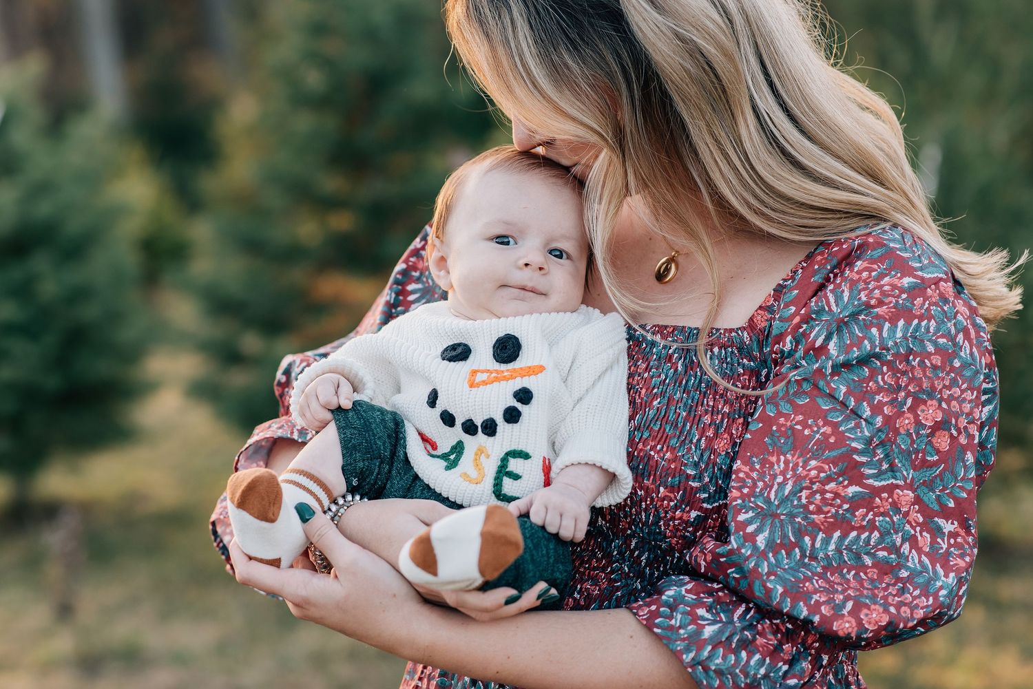A close up image of a newborn baby wearing a snowman sweater at a tree farm for a holiday mini session.