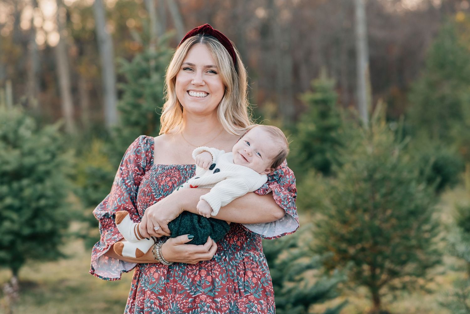 Mother wearing a red dress holding her newborn at a tree farm in Monmouth county NJ.