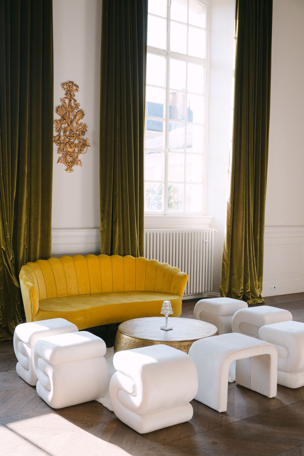 Modern event space with yellow curved sofa and white modular seating against dark curtained windows.