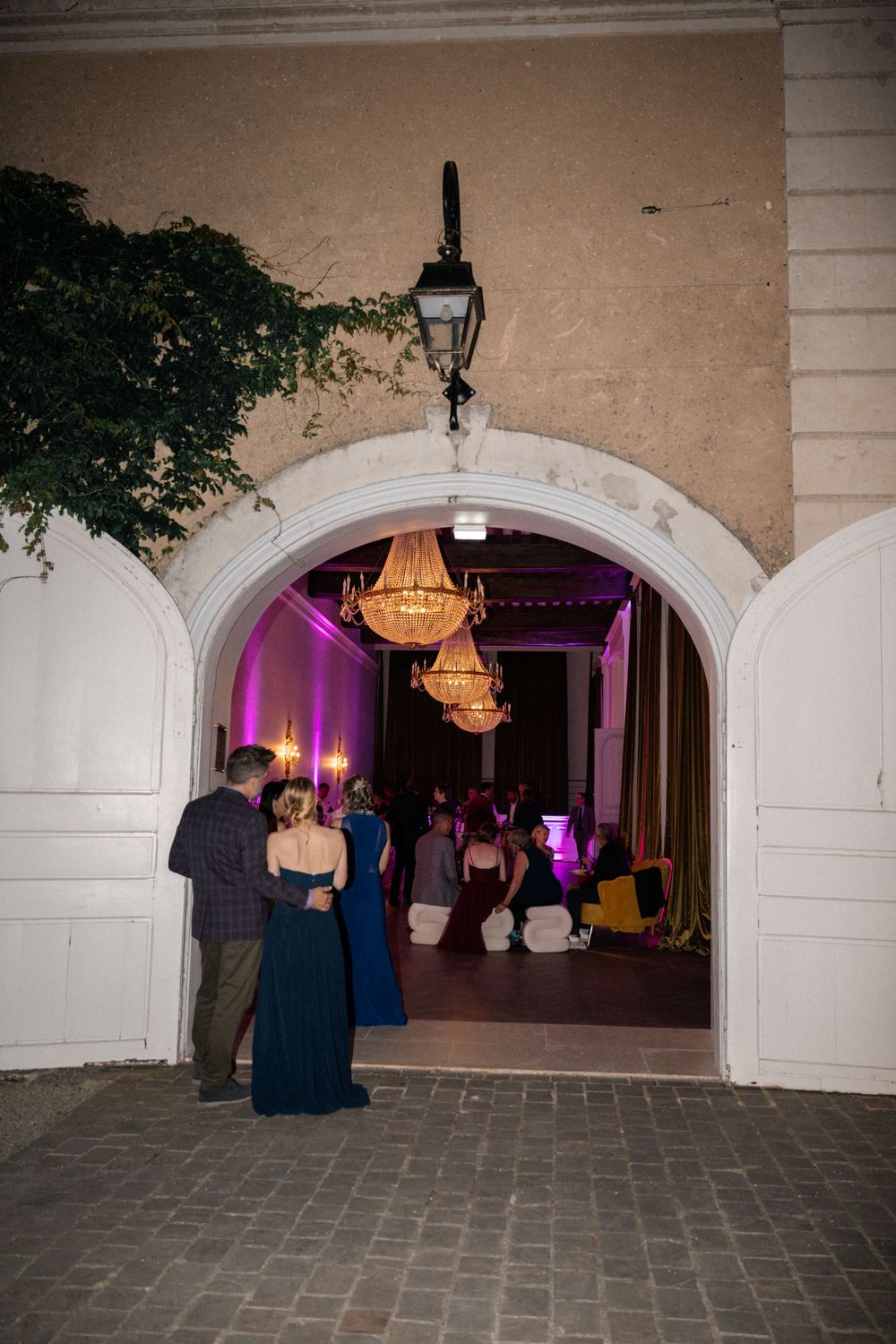 Arched entryway with purple uplighting and chandeliers leading into an elegant venue space.