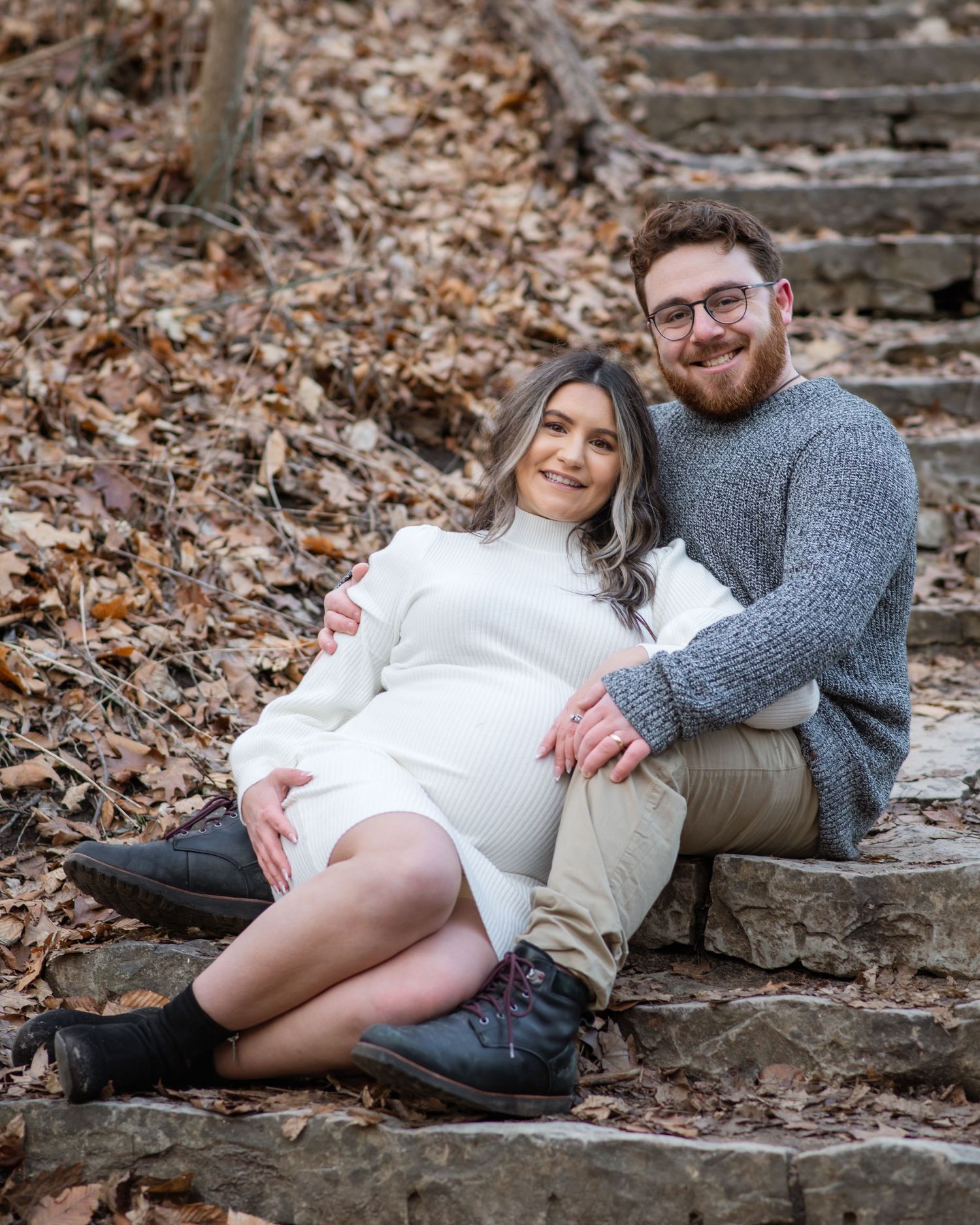 A couple relaxes together on stone steps covered in fallen autumn leaves during an outdoor photo session.