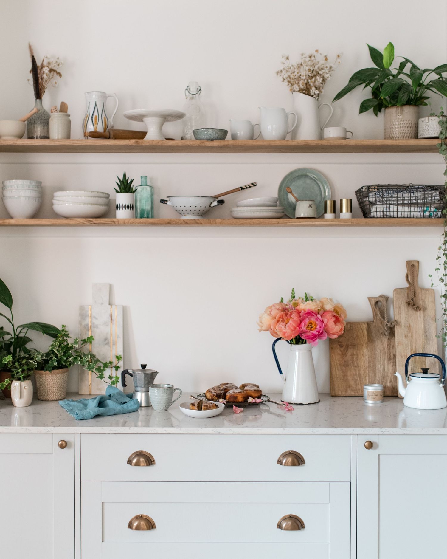 A bright modern kitchen with white cabinets, wooden floating shelves, and decorative items displayed on open shelving.