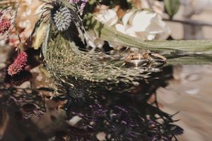 Dos anillos dorados sobre superficie reflectante rodeados de flores y hojas verdes, fotógrafo en País Vasco