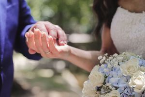 Manos entrelazadas con ramo de rosas blancas y hortensias azules, en entorno natural, fotógrafia de boda