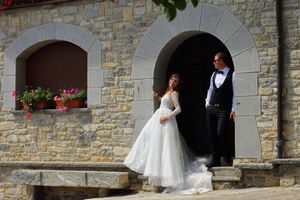 Pareja en atuendo de boda bajo arco de piedra, junto a fachada rústica con flores, fotografía de boda en Vitoria-Gasteiz