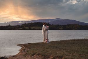 Pareja de la mano frente al lago al atardecer, con vestimenta tradicional y cielo vibrante, fotografía de boda realizada por BOAfoto