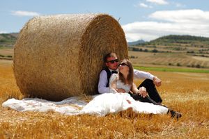Pareja en atuendo de boda sentada frente a paca de heno en campo rural con cielo nublado, fotógrafo boda, Bilbao, Vitoria, Donosti