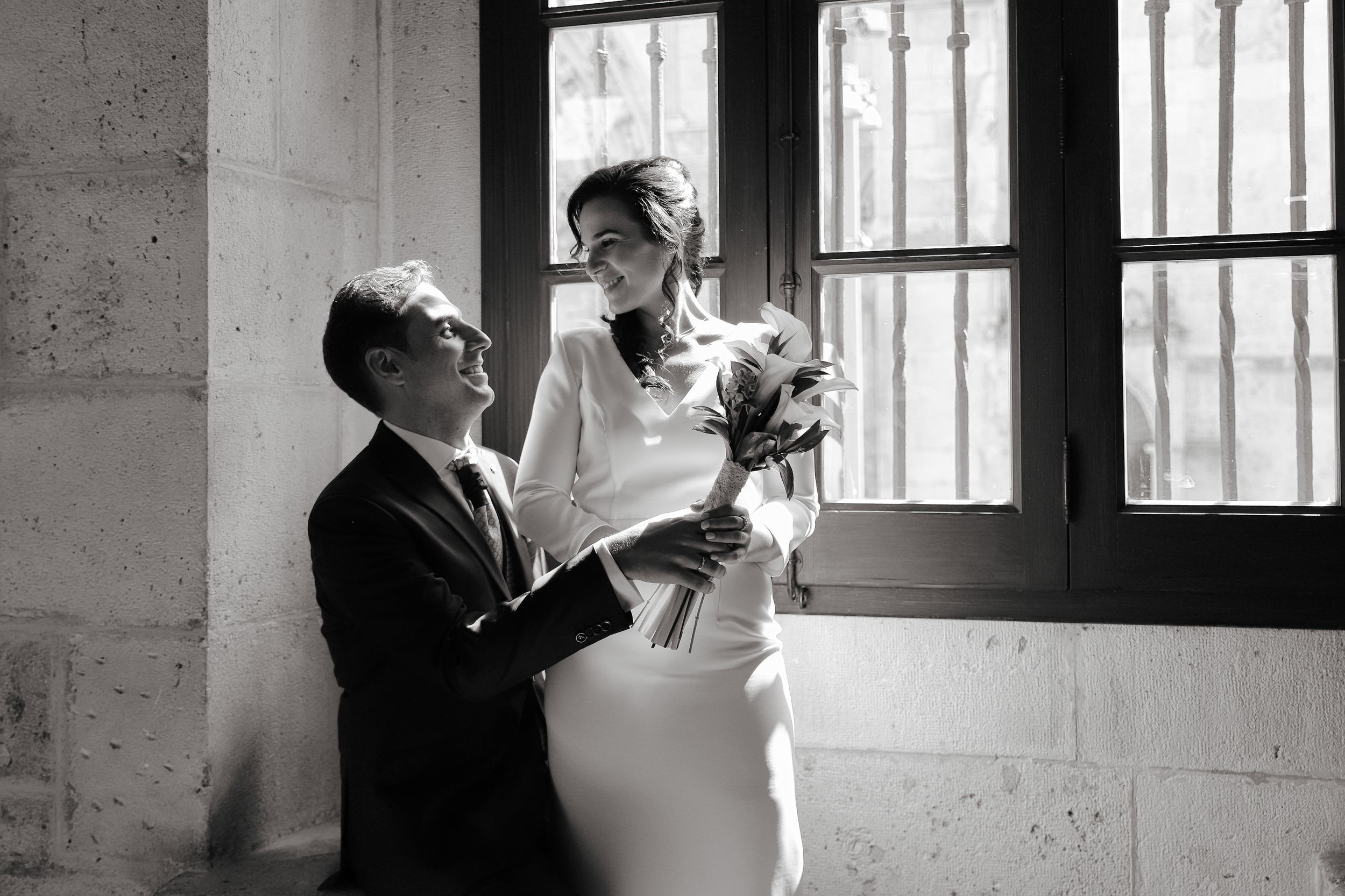 Novios en atuendo formal junto a ventana con luz natural, en interior de arquitectura histórica, fotógrafo boda en Burgos
