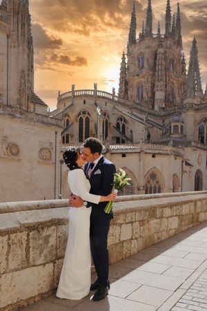 Pareja besándose frente a catedral de Burgos gótica al atardecer, con vestido blanco y ramo de calas, fotógrafo boda