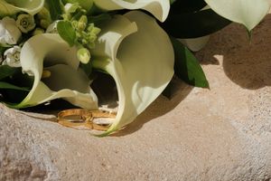 “Dos anillos dorados sobre piedra junto a ramo de calas blancas en luz suave, fotógrafo boda en Burgos