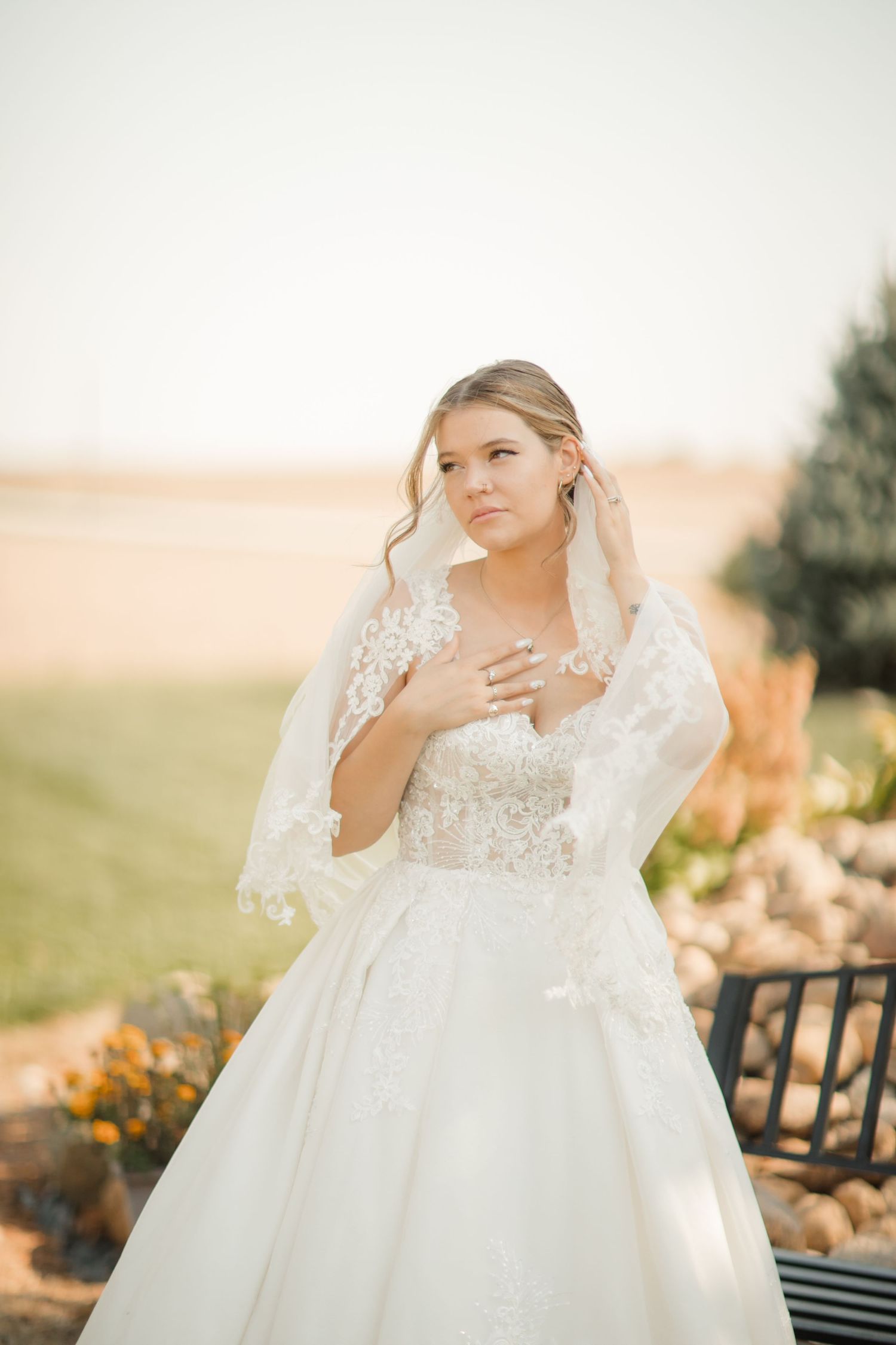 A bride in a white lace wedding gown poses outdoors during golden hour in a dreamy garden setting.