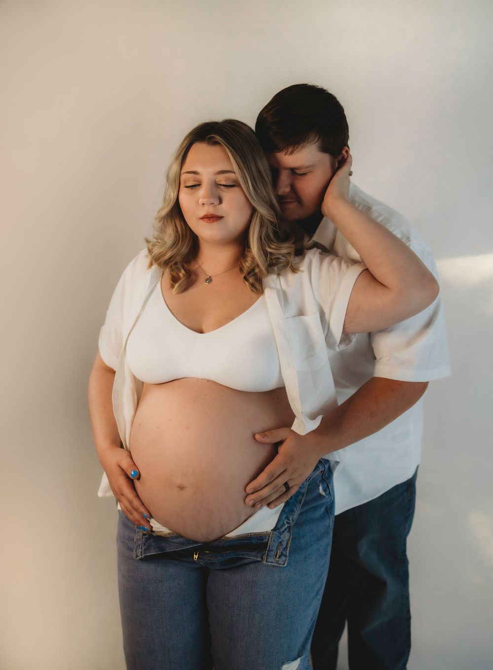 Couple embracing during maternity photoshoot against white background in studio.