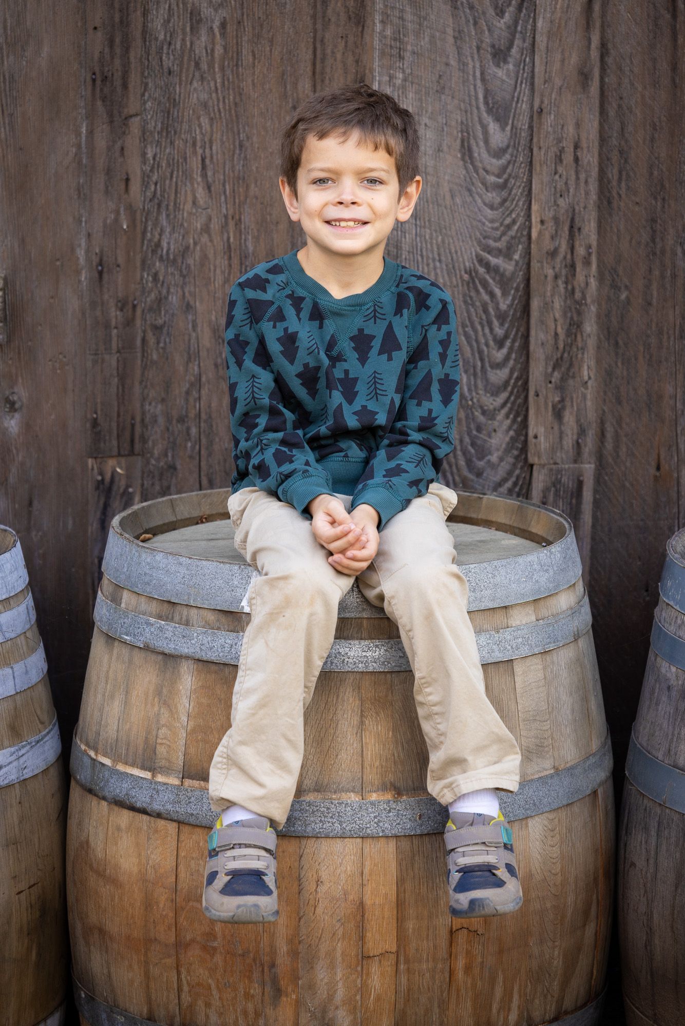 A child sits on a wooden wine barrel against a rustic wooden wall at San Jose family photo session