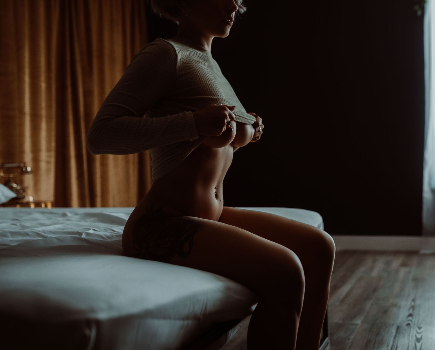 Woman in a sweater lounges on dark leather couch in moody lighting with Minnesota boudoir photography.