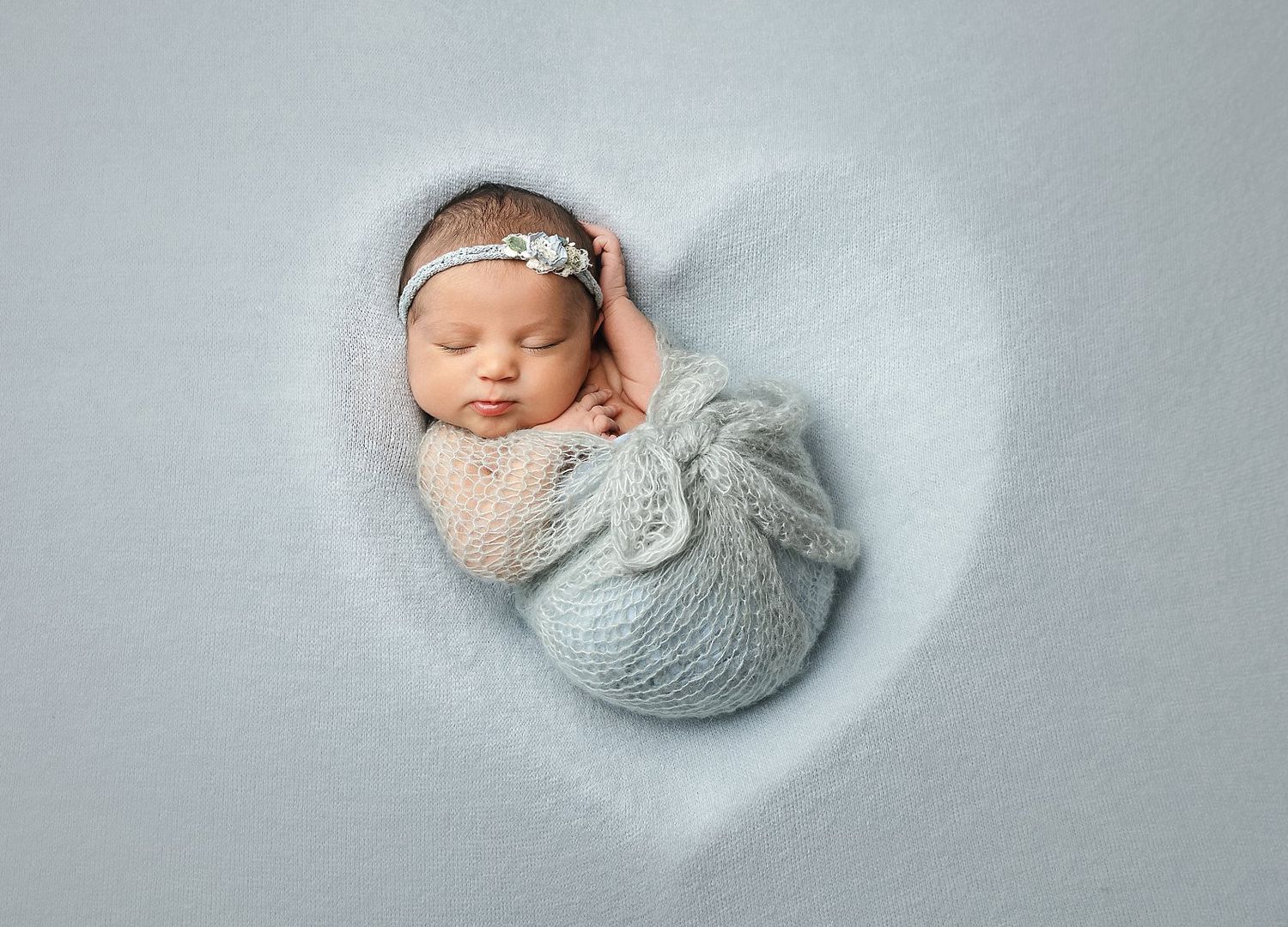 Wrapped newborn baby posed in heart shape on neutral backdrop in Austin newborn studio