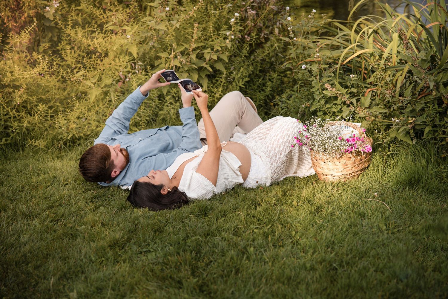 Pregnant couple relaxing and lying down in green grass on a sunny summer day in Vondelpark