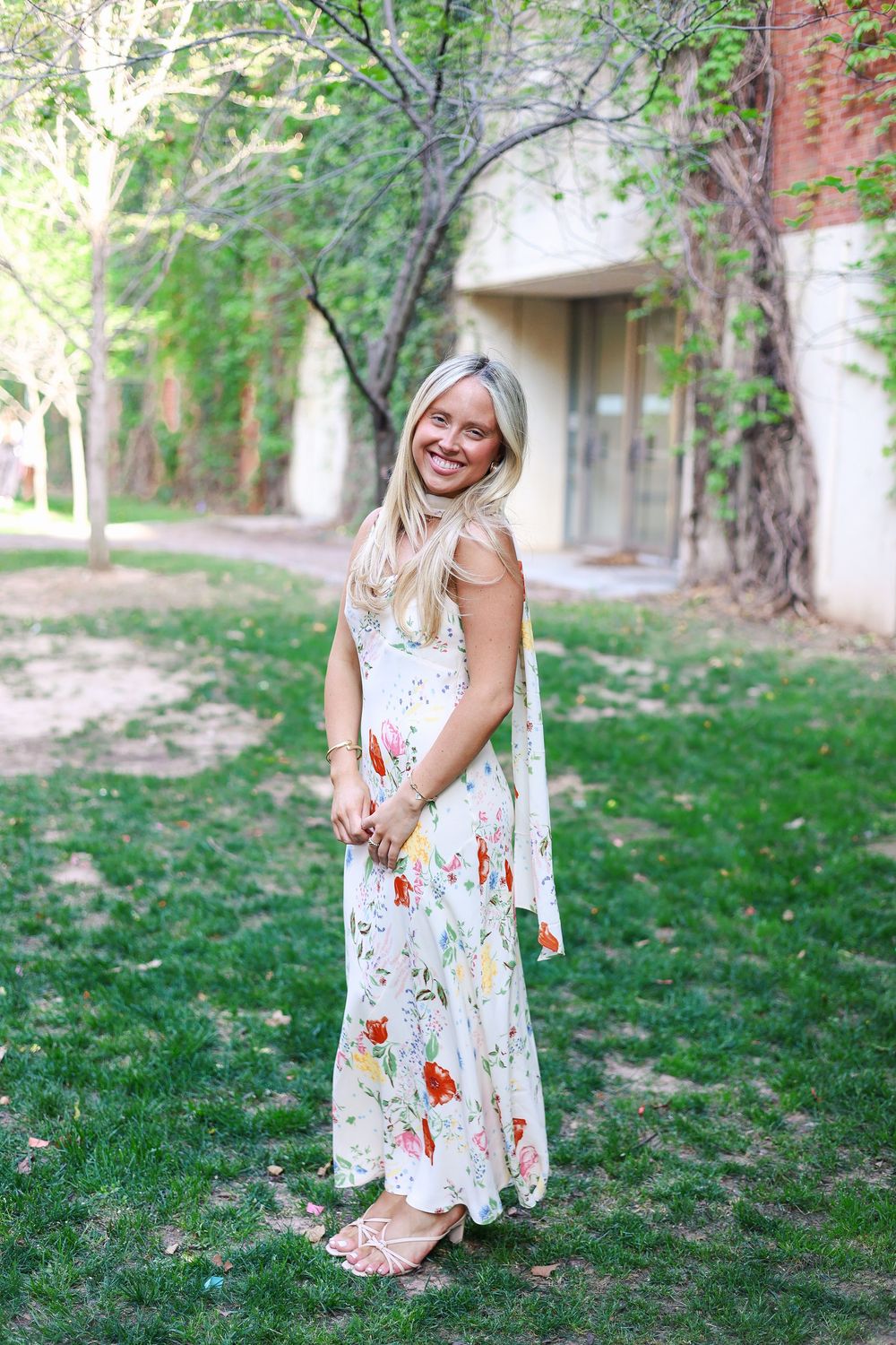 A floral sundress flows gracefully in a series of outdoor portraits taken on a grassy lawn near brick buildings.