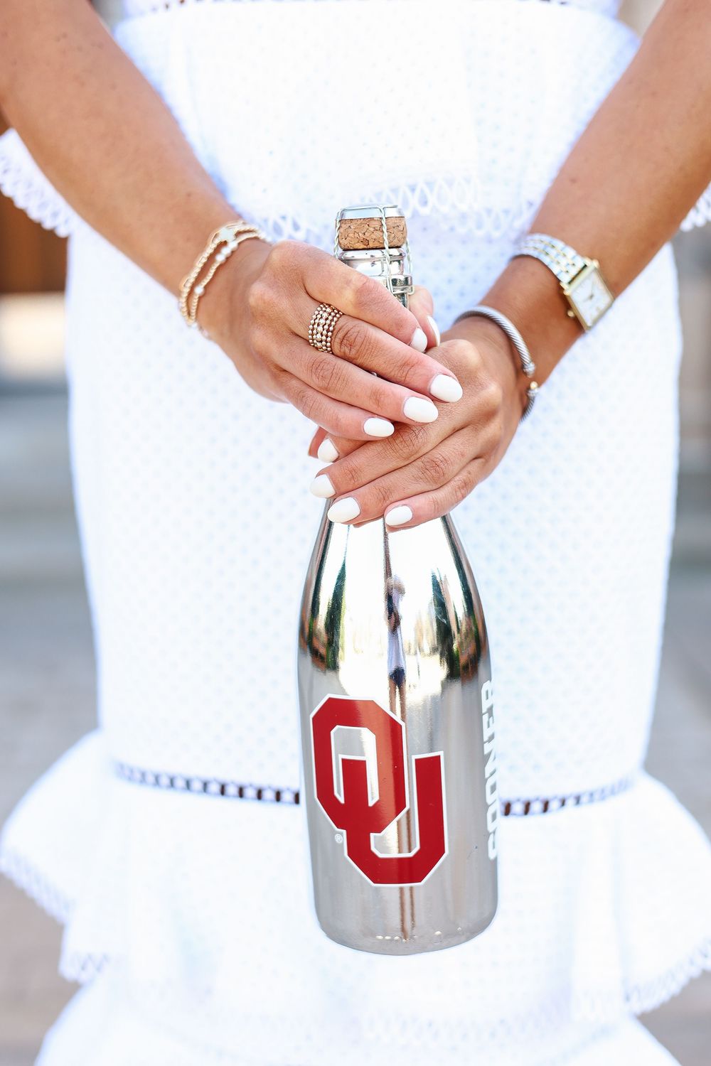 Close-up shots of hands holding a silver tumbler with red OU logo against a white dress background.
