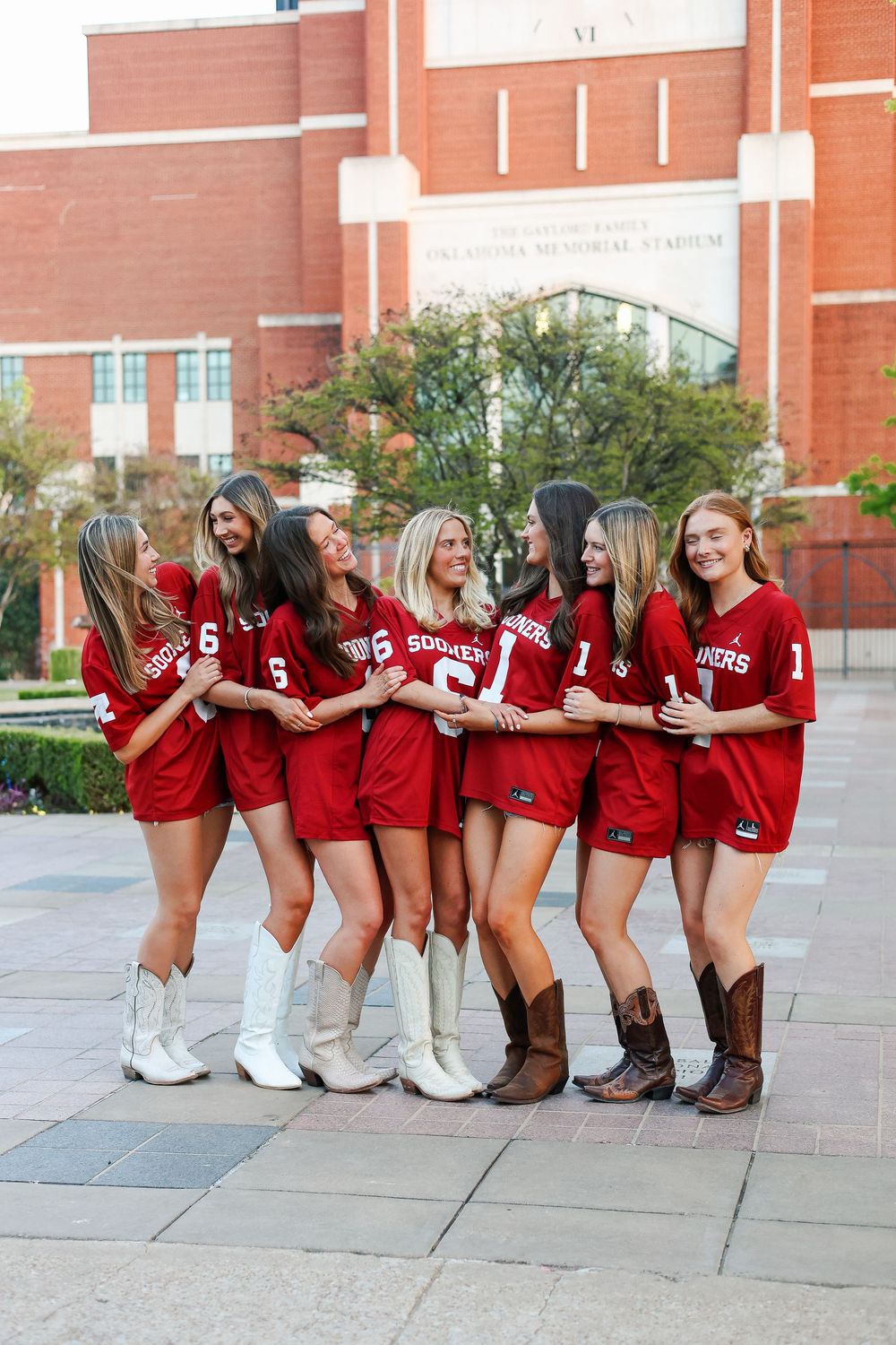 A group in matching red jerseys sits in a line on a concrete walkway outside a brick building.