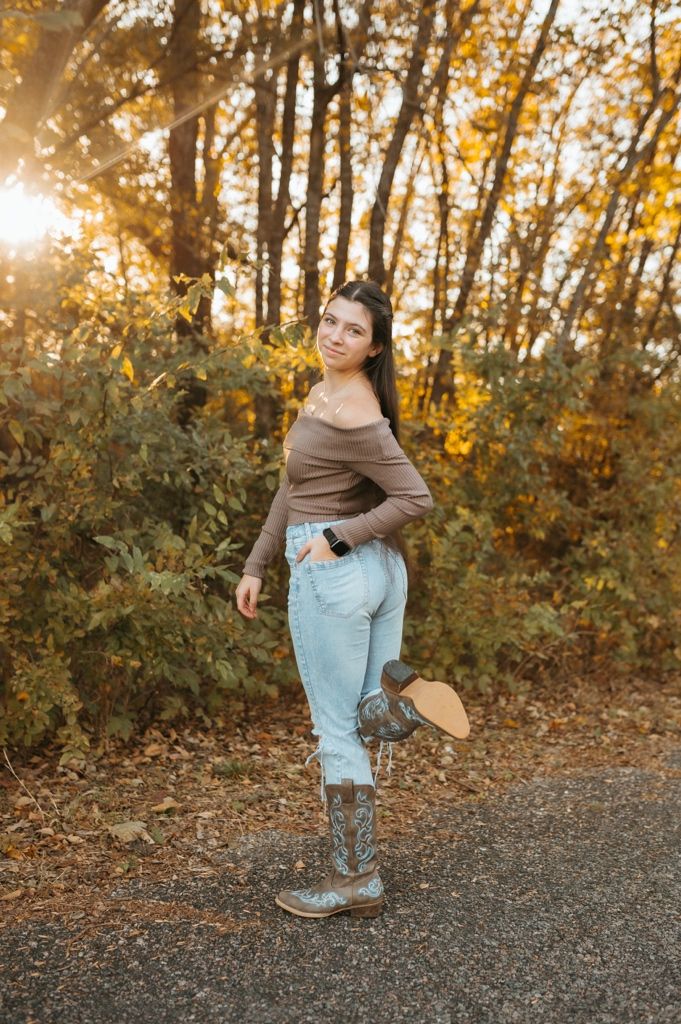 Figure in casual attire dances on gravel path surrounded by golden fall foliage.
