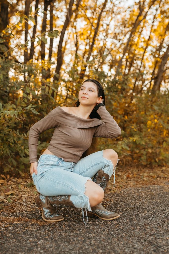 Relaxed outdoor portrait session featuring light denim and brown sweater against fall foliage.