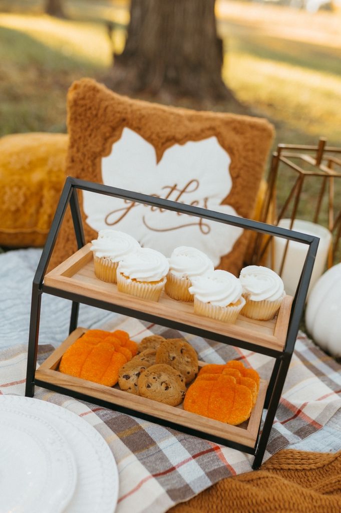 A rustic display of cupcakes and pastries on a wooden tiered stand with plaid cloth and autumn decor.