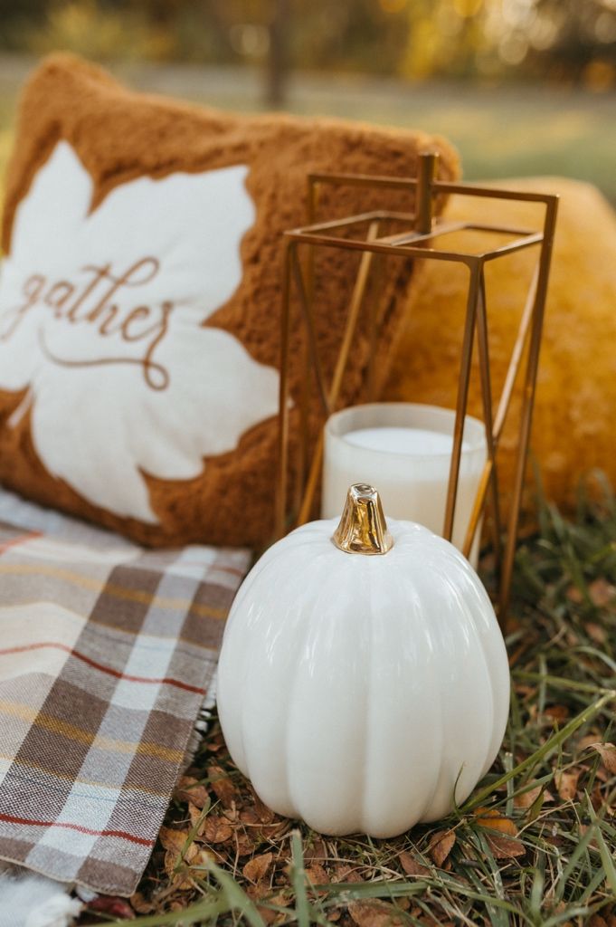 White decorative pumpkin on plaid fabric with greenery creates a cozy autumn vignette.