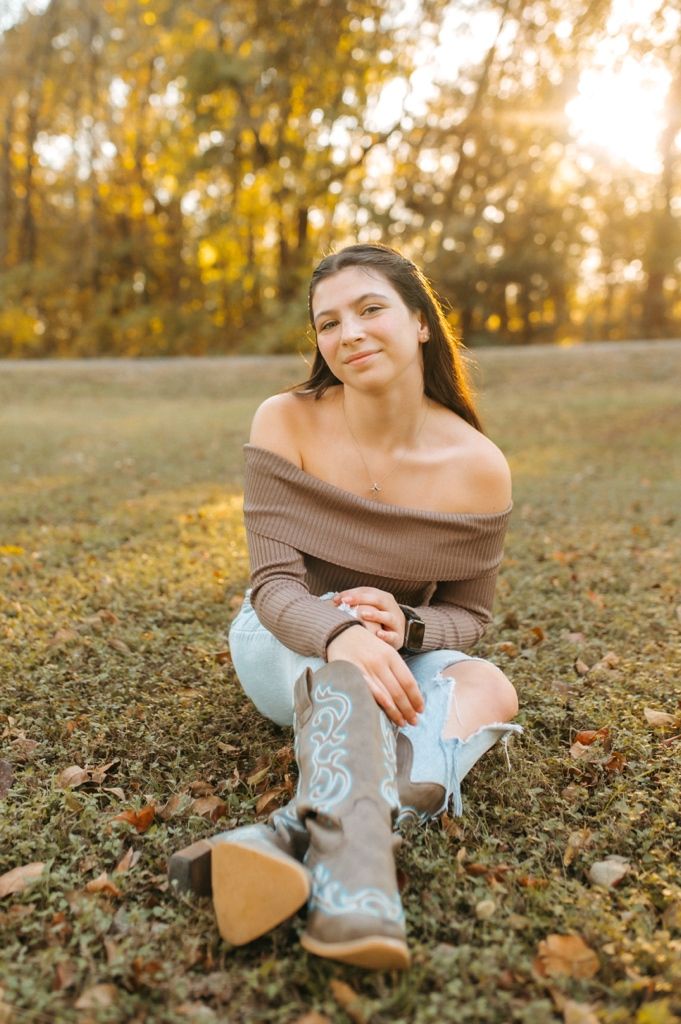 Outdoor autumn portrait with brown off-shoulder sweater and decorative cowboy boots in golden sunlit field.
