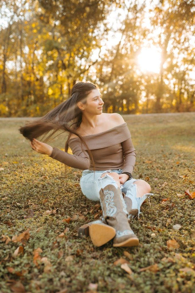 Person in brown sweater and jeans laying in autumn leaves during golden hour sunset.