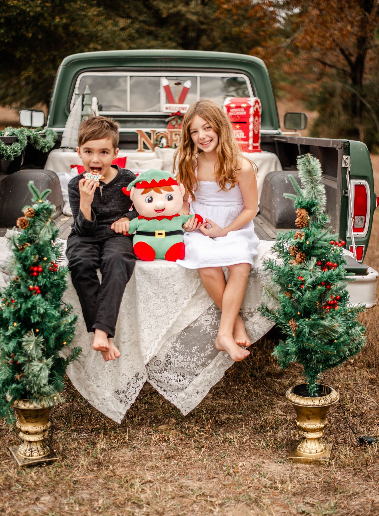 Children sitting on vintage pickup truck with Christmas wreaths and decorations during festive holiday photoshoot.