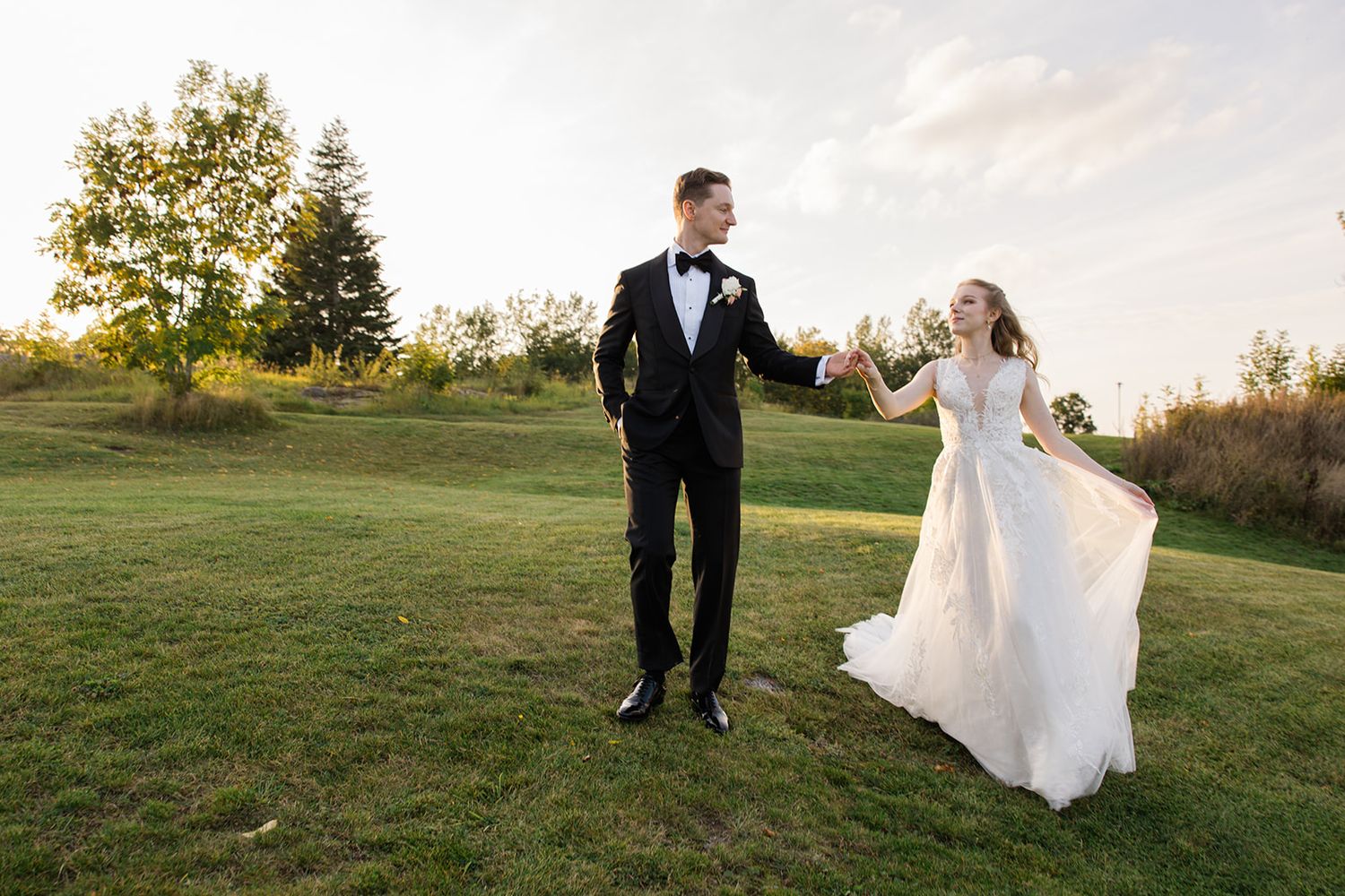 A bride and groom share a romantic moment at sunset in a grassy field during their wedding photo session.