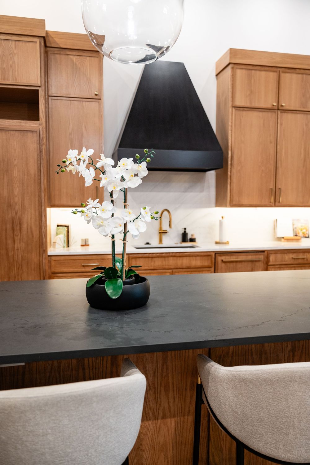 Modern kitchen design featuring wooden cabinets, black countertops, and white orchid decor with pendant lighting.