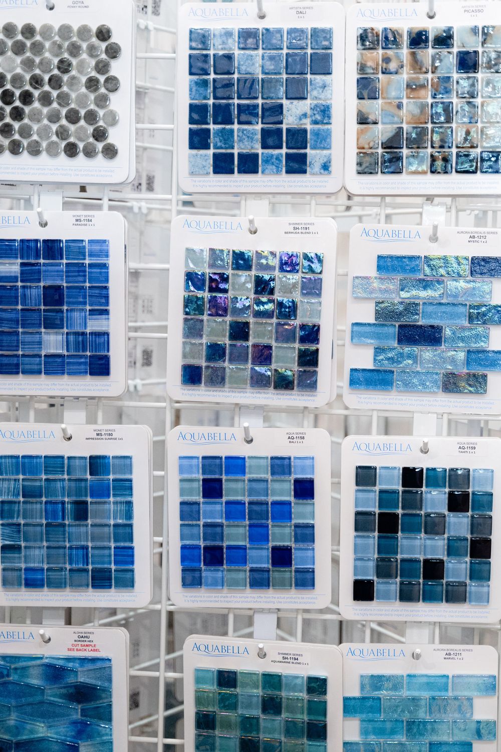 Rows of blue and white glass tile samples arranged on a wall display showcase various aquatic-inspired mosaic patterns.